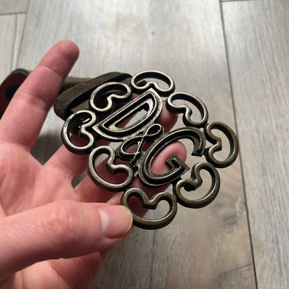 Dolce & Gabbana Green Suede Hearts Belt is made from very dark green suede with an orange leather interior featuring large dot detailing. The buckle is a metal D&G logo surrounded by eight heart shapes pointing outward, all finished in a dark, aged-looking metal tone. The belt comes with the original hologram tag attached.