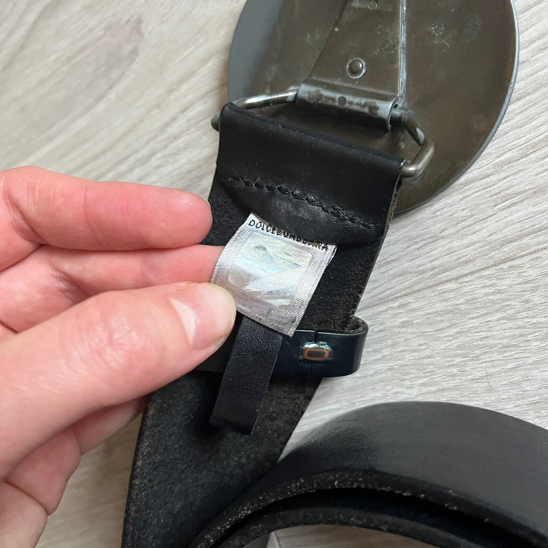 2000's Dolce & Gabbana black leather belt featuring a circular dark silver-tone metal buckle with the Italian flag and D&G logo in the center. The buckle is bordered by a navy ring with engraved text reading “Project And Design Conceived In Italy By Dolce & Gabbana”.