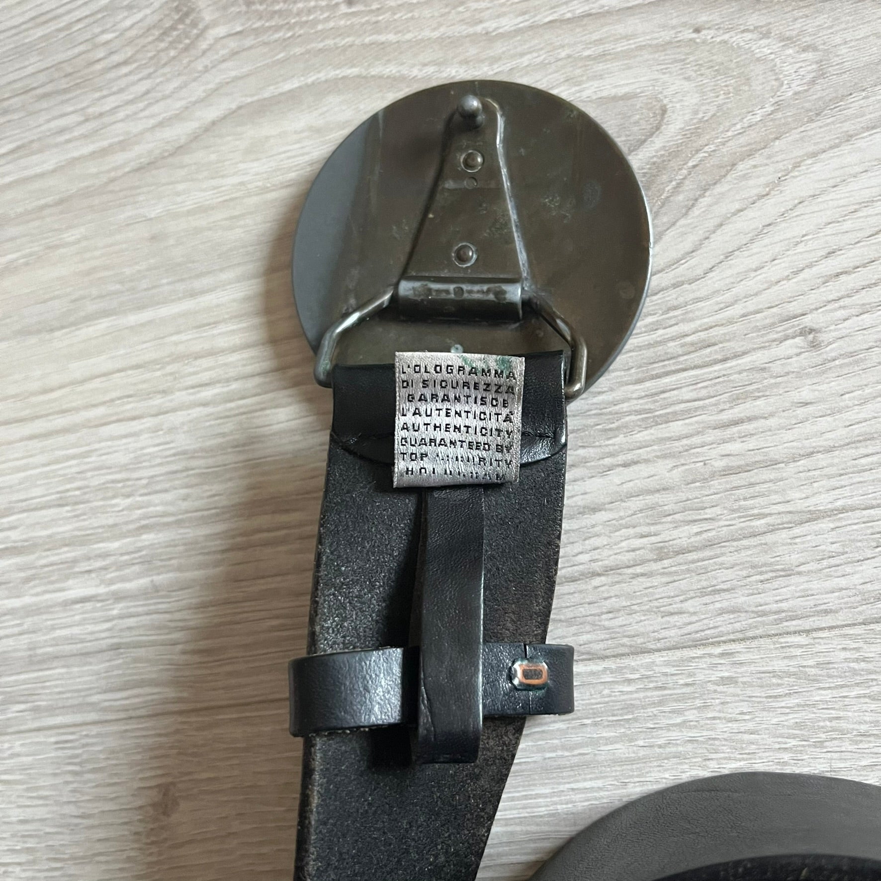 2000's Dolce & Gabbana black leather belt featuring a circular dark silver-tone metal buckle with the Italian flag and D&G logo in the center. The buckle is bordered by a navy ring with engraved text reading “Project And Design Conceived In Italy By Dolce & Gabbana”.