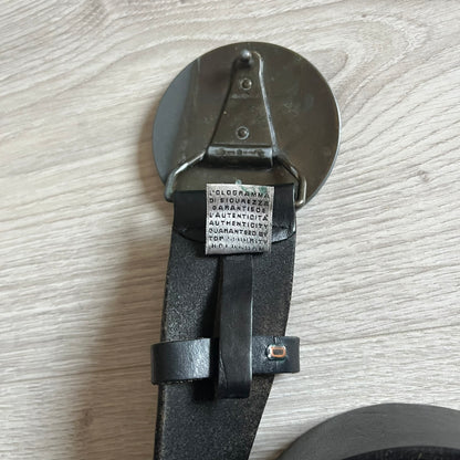 2000's Dolce & Gabbana black leather belt featuring a circular dark silver-tone metal buckle with the Italian flag and D&G logo in the center. The buckle is bordered by a navy ring with engraved text reading “Project And Design Conceived In Italy By Dolce & Gabbana”.