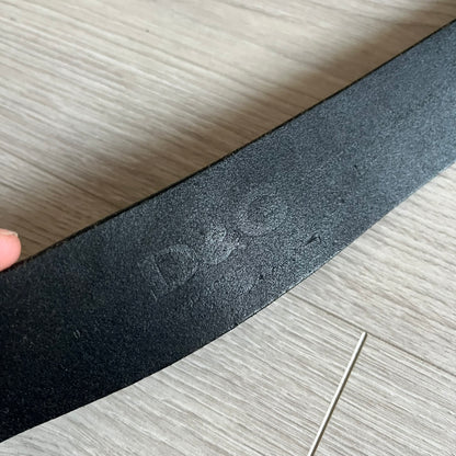 2000's Dolce & Gabbana black leather belt featuring a circular dark silver-tone metal buckle with the Italian flag and D&G logo in the center. The buckle is bordered by a navy ring with engraved text reading “Project And Design Conceived In Italy By Dolce & Gabbana”.