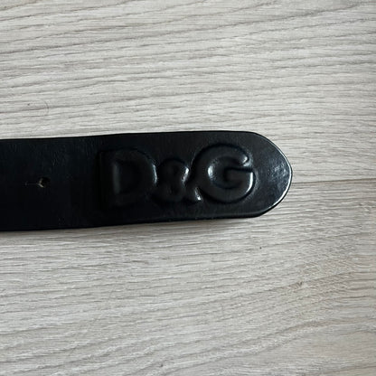 2000's Dolce & Gabbana black leather belt featuring a circular dark silver-tone metal buckle with the Italian flag and D&G logo in the center. The buckle is bordered by a navy ring with engraved text reading “Project And Design Conceived In Italy By Dolce & Gabbana”.