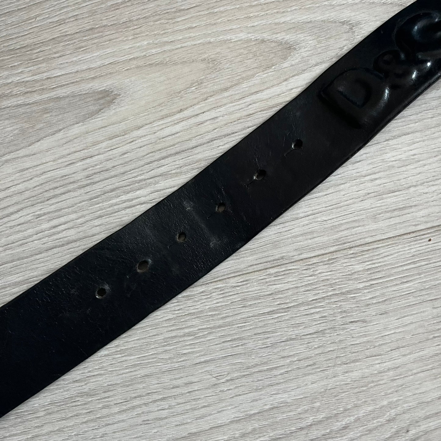 2000's Dolce & Gabbana black leather belt featuring a circular dark silver-tone metal buckle with the Italian flag and D&G logo in the center. The buckle is bordered by a navy ring with engraved text reading “Project And Design Conceived In Italy By Dolce & Gabbana”.