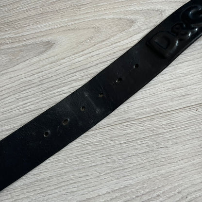 2000's Dolce & Gabbana black leather belt featuring a circular dark silver-tone metal buckle with the Italian flag and D&G logo in the center. The buckle is bordered by a navy ring with engraved text reading “Project And Design Conceived In Italy By Dolce & Gabbana”.