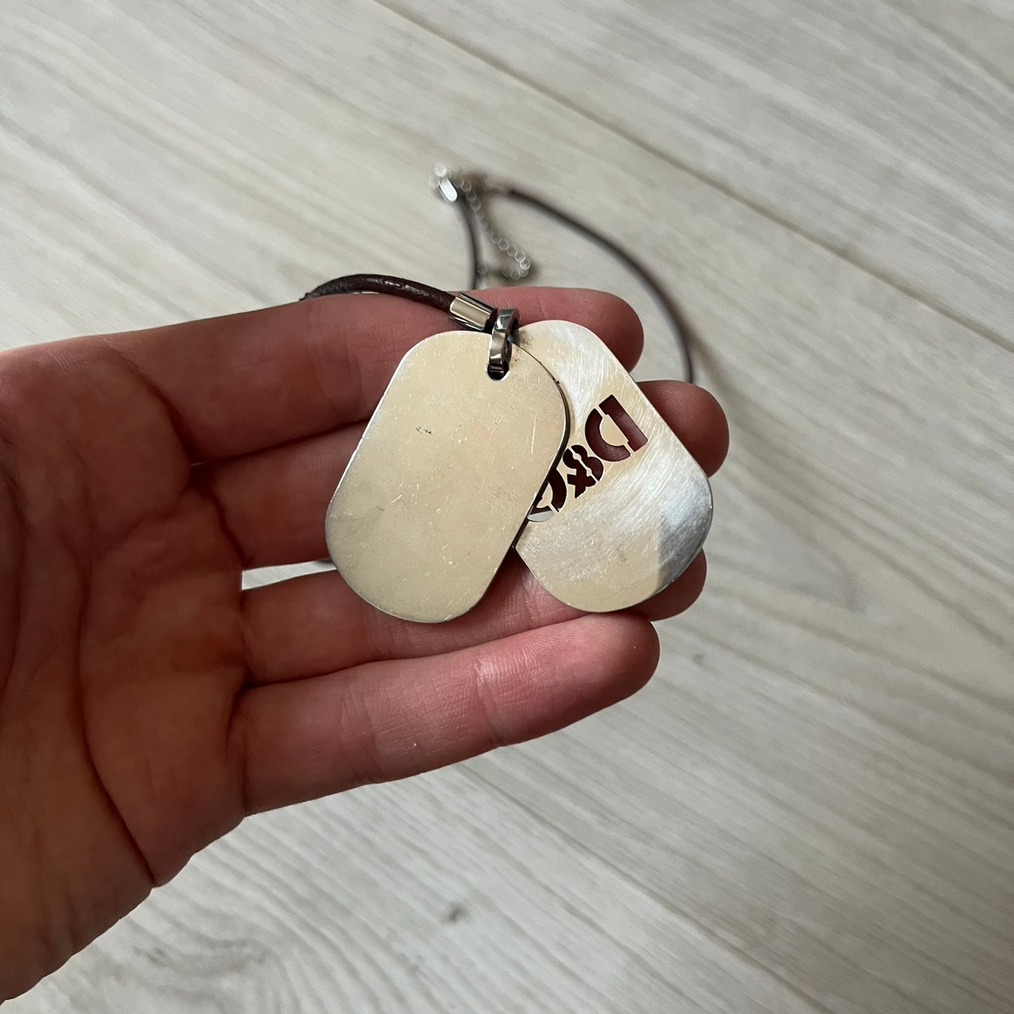 Dolce &amp; Gabbana double dog tag necklace featuring two layered pendants: a italy flag tag underneath and a silver-tone tag on top with a cut-out D&amp;G logo revealing the tricolor tag beneath. Designed with brown leather-ish string.