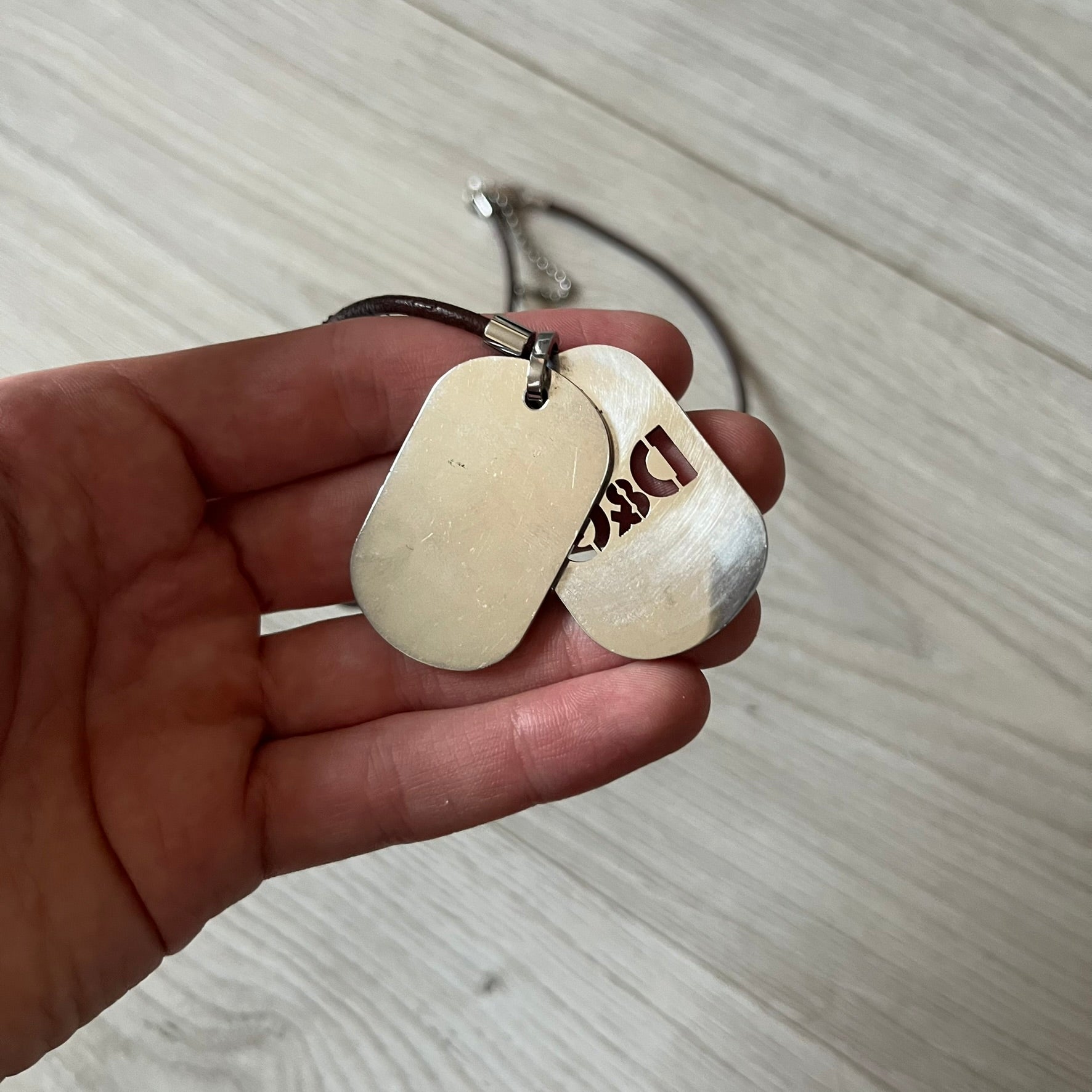 Dolce &amp; Gabbana double dog tag necklace featuring two layered pendants: a italy flag tag underneath and a silver-tone tag on top with a cut-out D&amp;G logo revealing the tricolor tag beneath. Designed with brown leather-ish string.