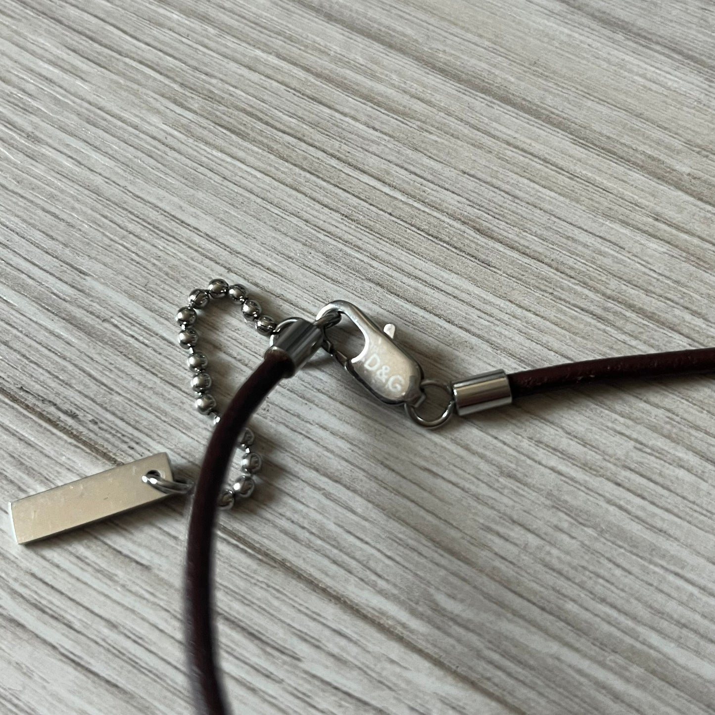 Dolce &amp; Gabbana double dog tag necklace featuring two layered pendants: a italy flag tag underneath and a silver-tone tag on top with a cut-out D&amp;G logo revealing the tricolor tag beneath. Designed with brown leather-ish string.