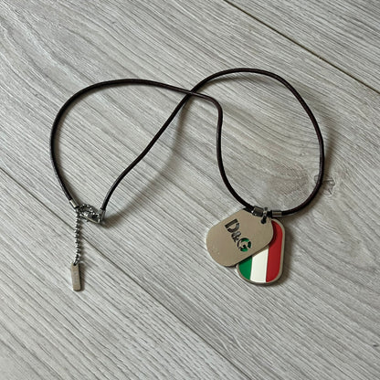 Dolce &amp; Gabbana double dog tag necklace featuring two layered pendants: a italy flag tag underneath and a silver-tone tag on top with a cut-out D&amp;G logo revealing the tricolor tag beneath. Designed with brown leather-ish string.