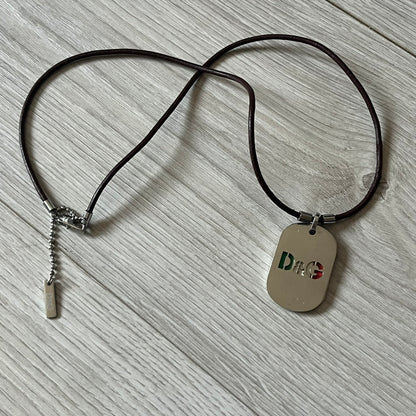 Dolce &amp; Gabbana double dog tag necklace featuring two layered pendants: a italy flag tag underneath and a silver-tone tag on top with a cut-out D&amp;G logo revealing the tricolor tag beneath. Designed with brown leather-ish string.