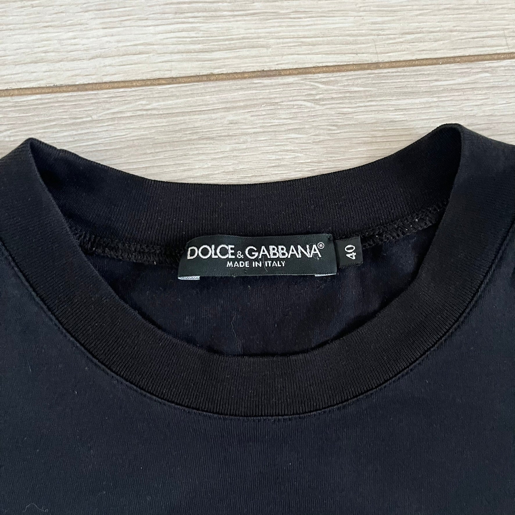 This Dolce &amp; Gabbana James Dean Black Tee features a premium Italian-made cotton construction with a front portrait of James. The design includes pretty big white/grey “James Dean” text across the upper back. The t-shirt celebrates the lasting influence of James Dean, a defining figure of mid-century cinema.