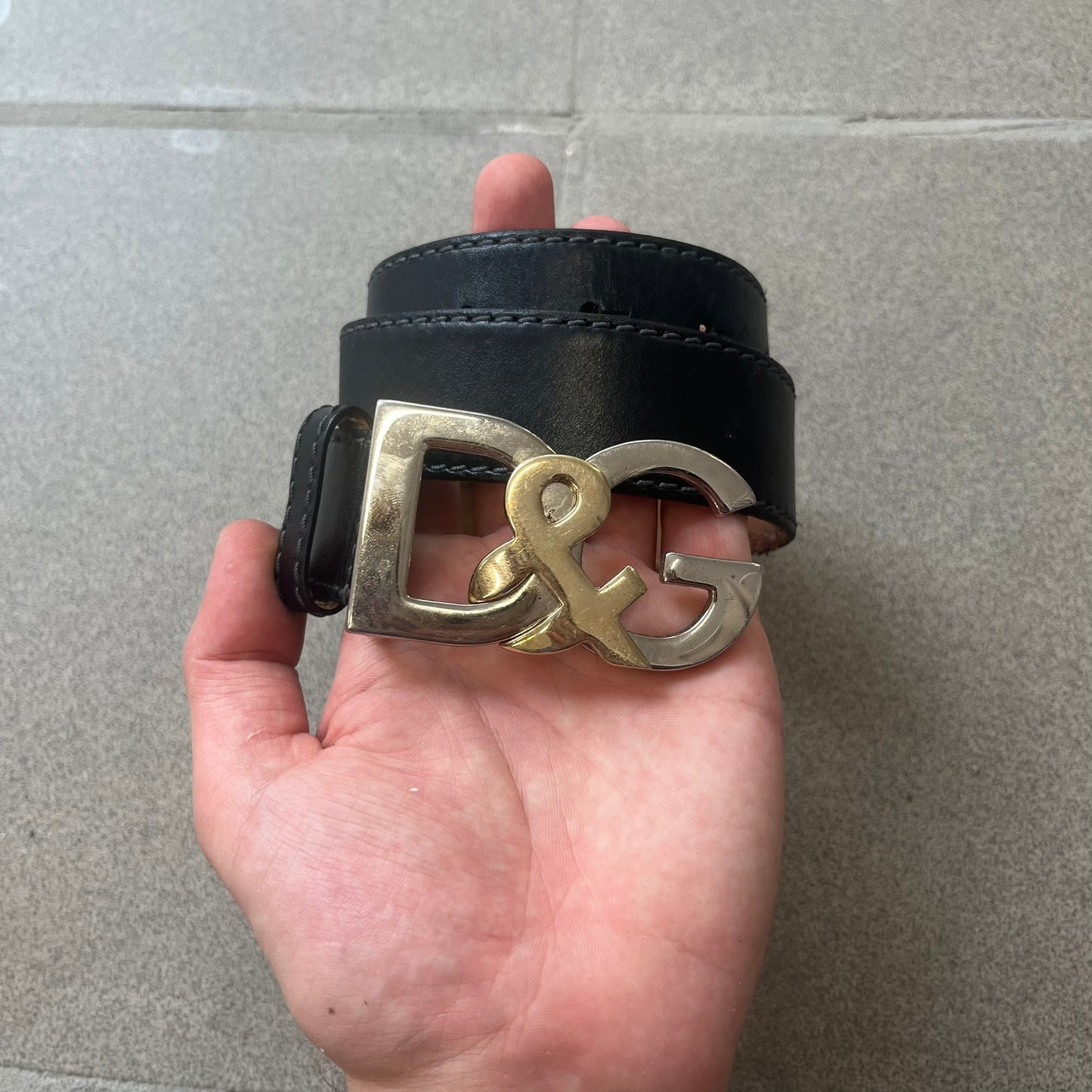 Dolce &amp; Gabbana Kids Logo Black Leather Belt features a black leather strap with a cutout DG logo buckle. The buckle combines a silver-tone “DG” design with a gold-tone ampersand detail. Made in Italy, the belt is crafted from 100% leather.
