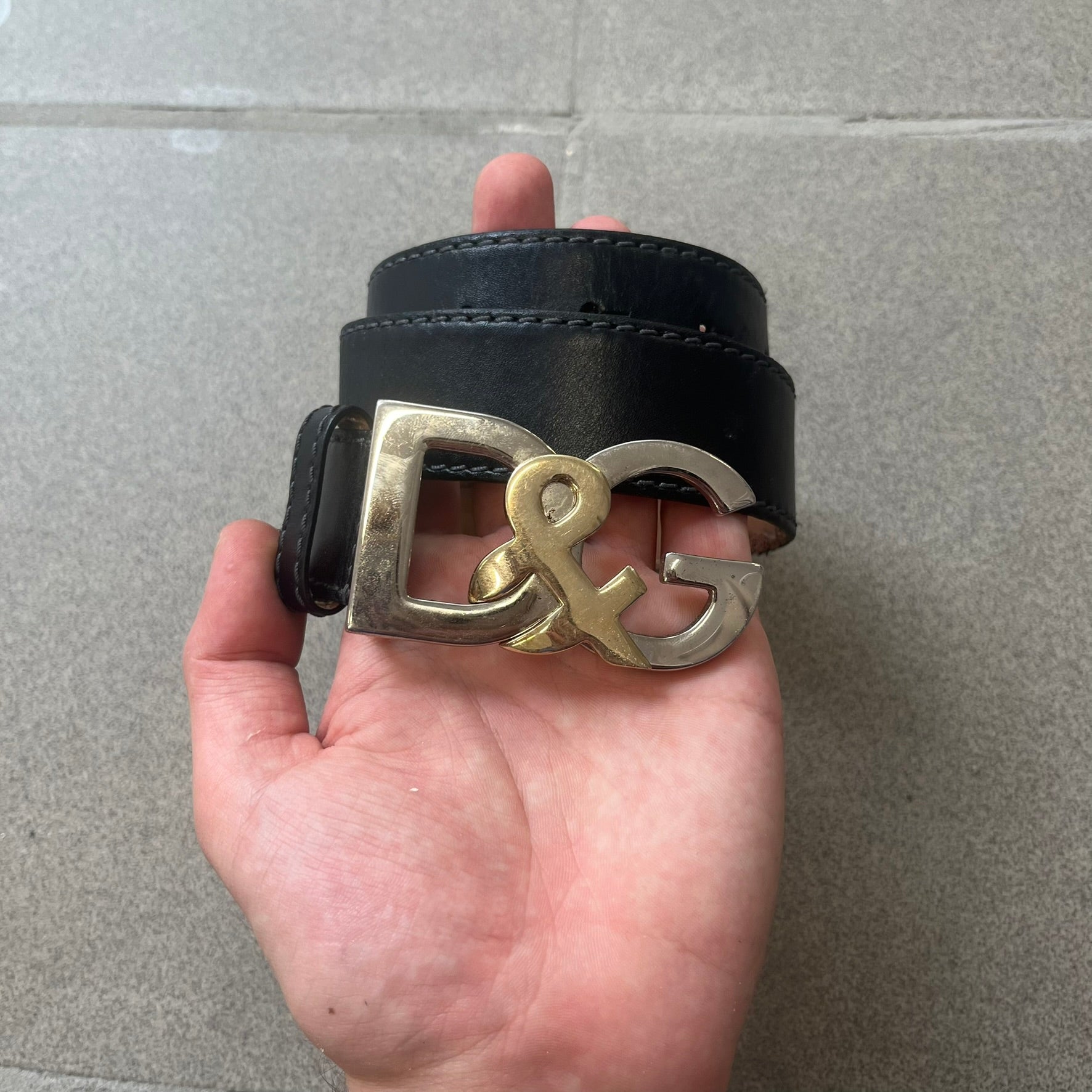 Dolce &amp; Gabbana Kids Logo Black Leather Belt features a black leather strap with a cutout DG logo buckle. The buckle combines a silver-tone “DG” design with a gold-tone ampersand detail. Made in Italy, the belt is crafted from 100% leather.