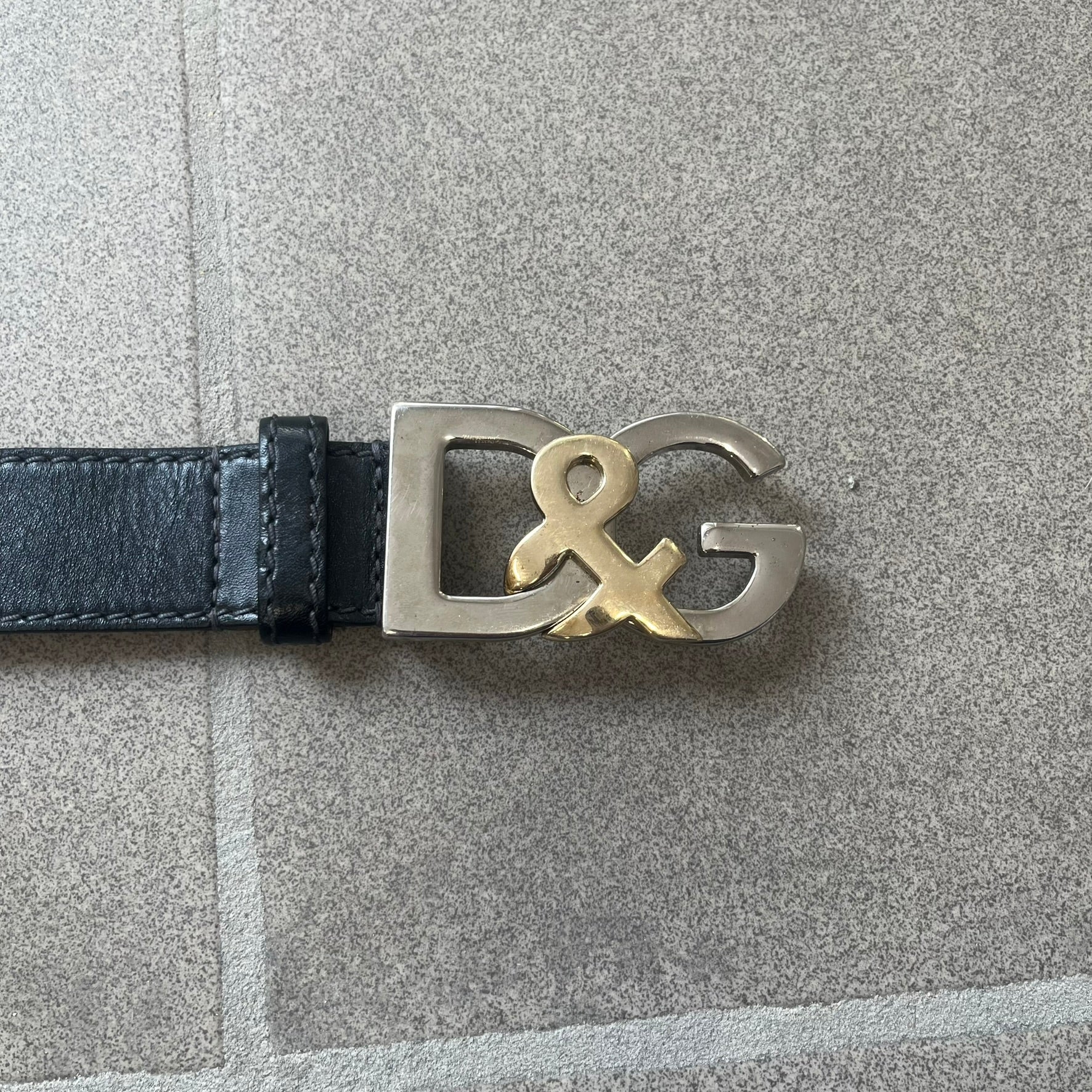 Dolce &amp; Gabbana Kids Logo Black Leather Belt features a black leather strap with a cutout DG logo buckle. The buckle combines a silver-tone “DG” design with a gold-tone ampersand detail. Made in Italy, the belt is crafted from 100% leather.