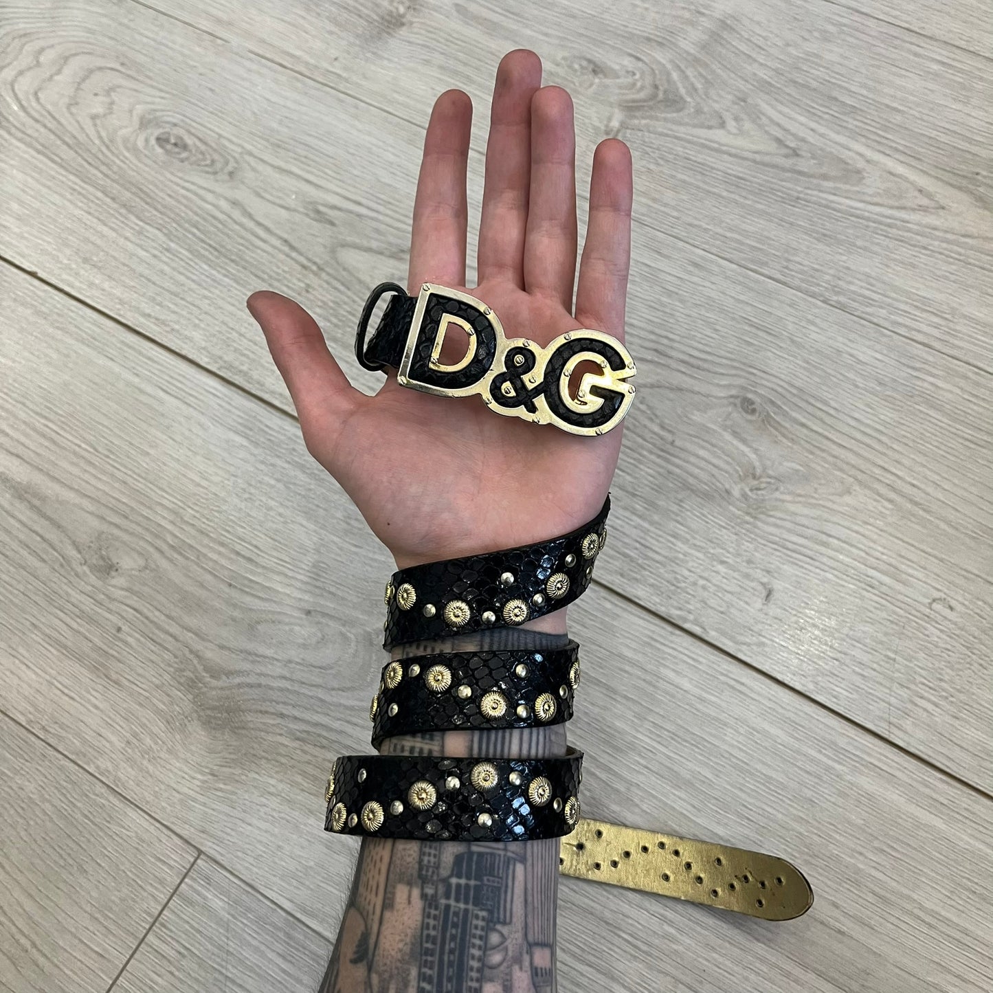 Dolce &amp; Gabbana Leather Studded Belt in black textured leather with a scaled, snake-like finish. The belt features gold stud detailing arranged in a clean pattern and a matching black D&amp;G buckle trimmed with gold hardware and exposed screws. The interior is finished in gold, adding a refined contrast to the overall design.