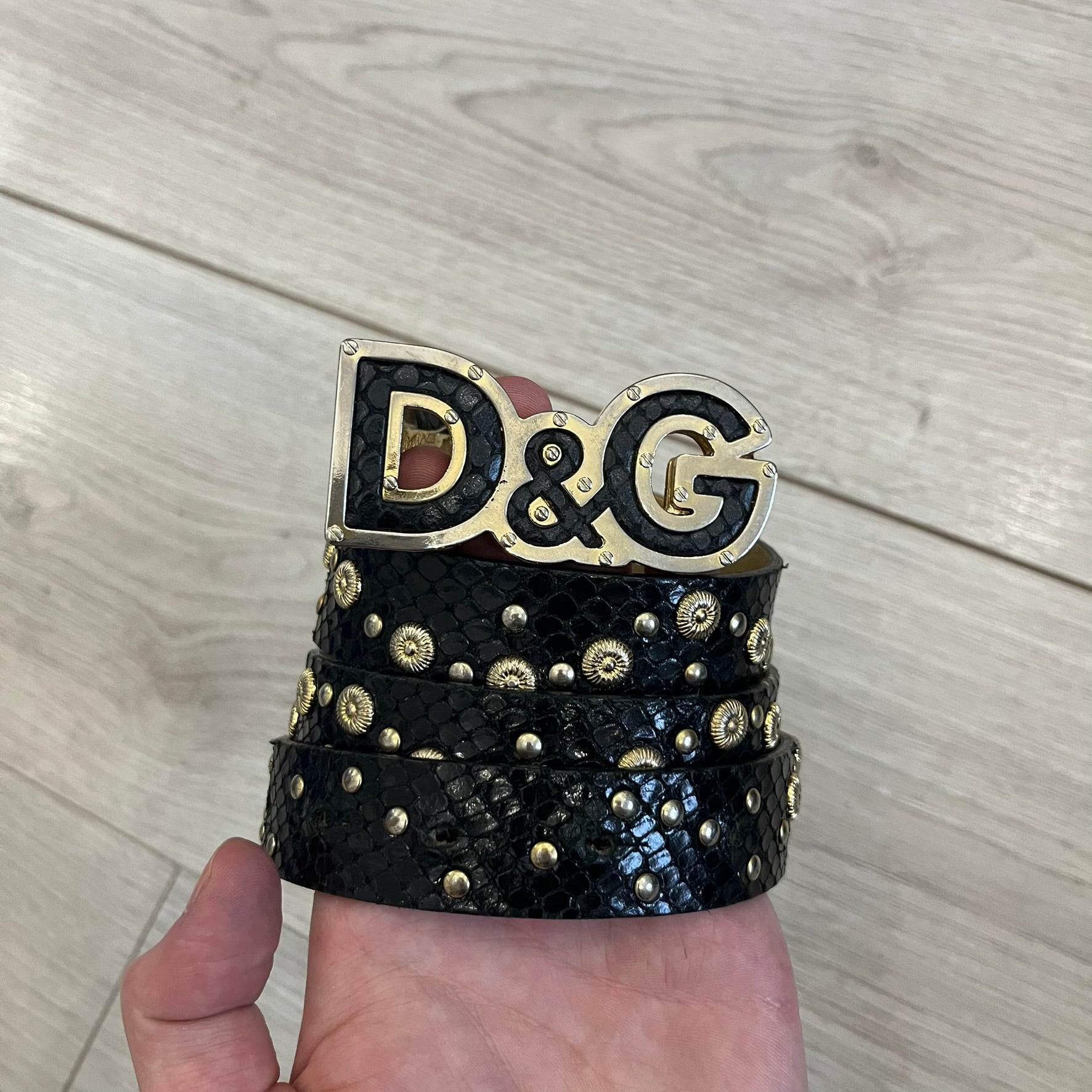 Dolce &amp; Gabbana Leather Studded Belt in black textured leather with a scaled, snake-like finish. The belt features gold stud detailing arranged in a clean pattern and a matching black D&amp;G buckle trimmed with gold hardware and exposed screws. The interior is finished in gold, adding a refined contrast to the overall design.