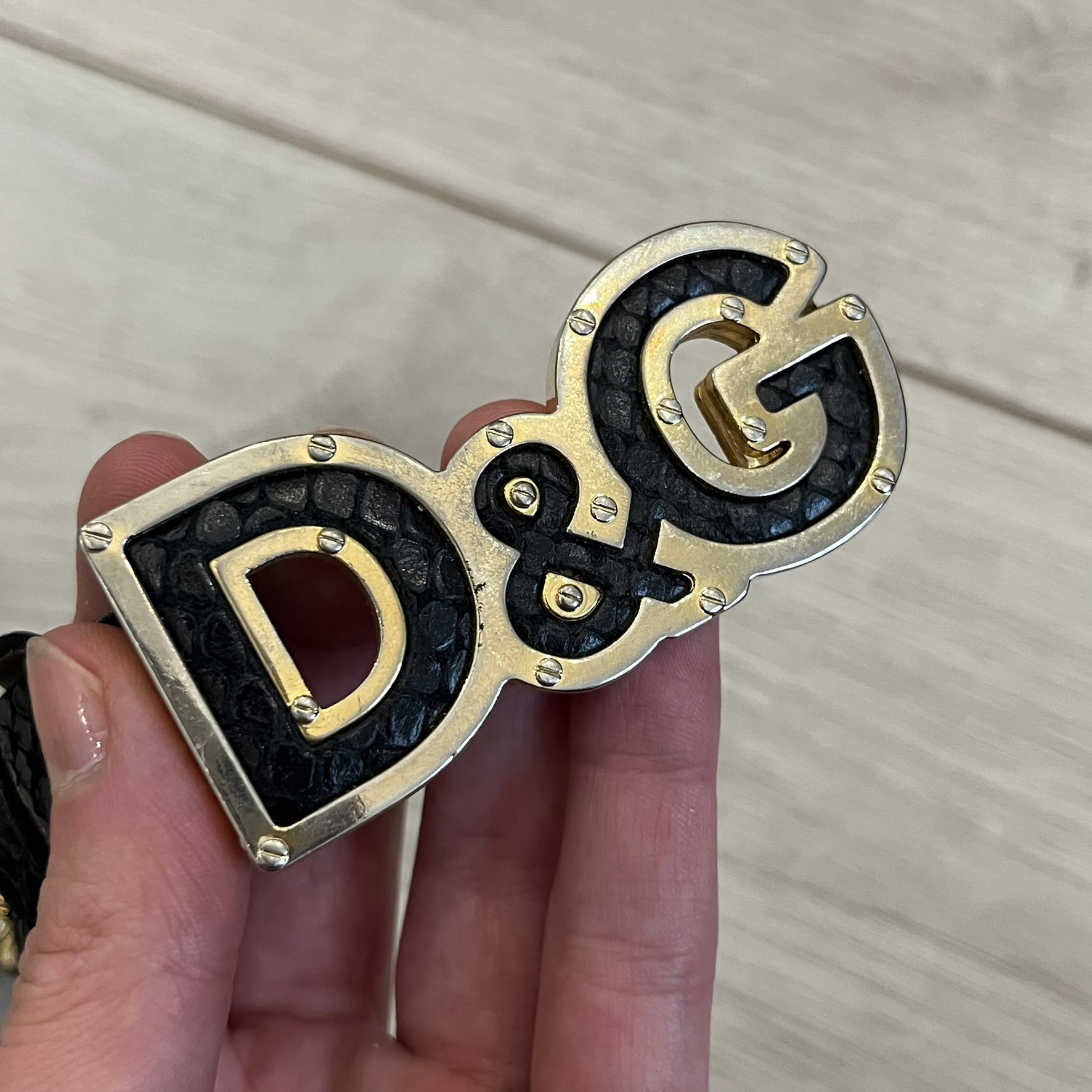 Dolce &amp; Gabbana Leather Studded Belt in black textured leather with a scaled, snake-like finish. The belt features gold stud detailing arranged in a clean pattern and a matching black D&amp;G buckle trimmed with gold hardware and exposed screws. The interior is finished in gold, adding a refined contrast to the overall design.