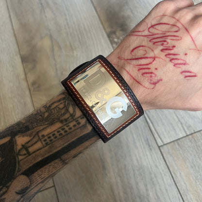 Dolce & Gabbana Logo Leather Bracelet is a leather bracelet made in Italy. It features an adjustable closure and a large stainless steel plaque on the front. The plaque is engraved with the D&G logo and Dolce & Gabbana text. Silver-tone hardware is used throughout the bracelet.