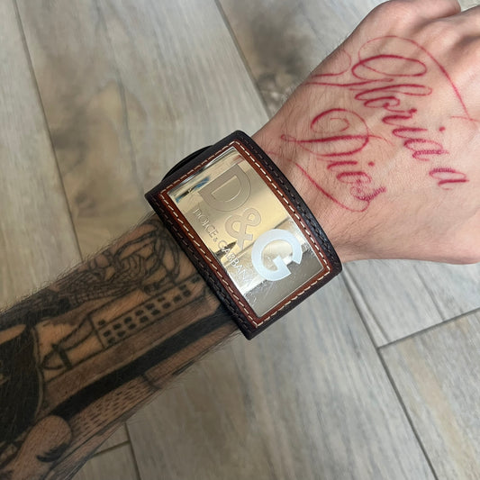 Dolce & Gabbana Logo Leather Bracelet is a leather bracelet made in Italy. It features an adjustable closure and a large stainless steel plaque on the front. The plaque is engraved with the D&G logo and Dolce & Gabbana text. Silver-tone hardware is used throughout the bracelet.