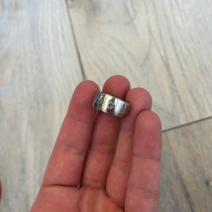 Dolce & Gabbana Logo Repeat Ring is a stainless steel ring featuring repeating engraved D&G logos around the entire band. The design is minimal and clean, focusing on subtle branded detailing and polished metal construction.