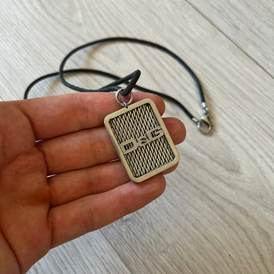 Hand holding a silver pendant with a textured design on a light wooden surface