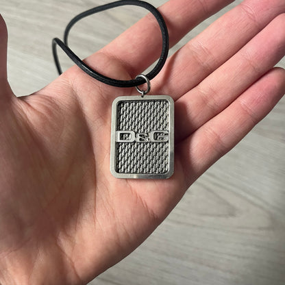 Dolce &amp; Gabbana Mesh Necklace featuring a stainless steel plate engraved with the D&amp;G logo, attached to a black leather cord. The reverse side displays a detailed grid-style mesh design. Model DJ0452, crafted with precision and industrial-inspired elegance.