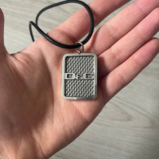 Dolce &amp; Gabbana Mesh Necklace featuring a stainless steel plate engraved with the D&amp;G logo, attached to a black leather cord. The reverse side displays a detailed grid-style mesh design. Model DJ0452, crafted with precision and industrial-inspired elegance.