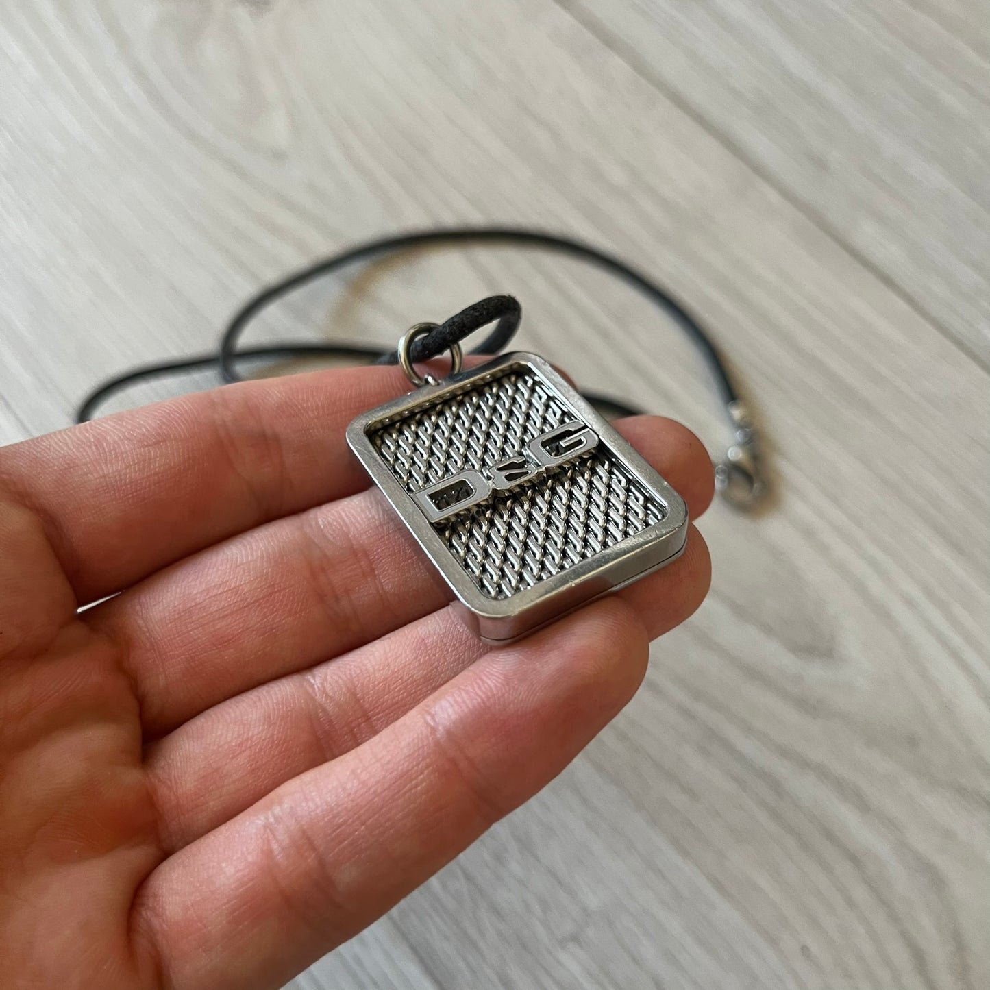 Silver pendant held in a hand with a light background