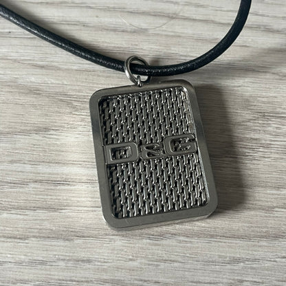Dolce &amp; Gabbana Mesh Necklace featuring a stainless steel plate engraved with the D&amp;G logo, attached to a black leather cord. The reverse side displays a detailed grid-style mesh design. Model DJ0452, crafted with precision and industrial-inspired elegance.
