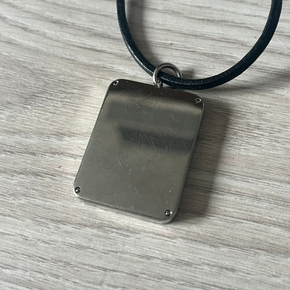 Dolce &amp; Gabbana Mesh Necklace featuring a stainless steel plate engraved with the D&amp;G logo, attached to a black leather cord. The reverse side displays a detailed grid-style mesh design. Model DJ0452, crafted with precision and industrial-inspired elegance.