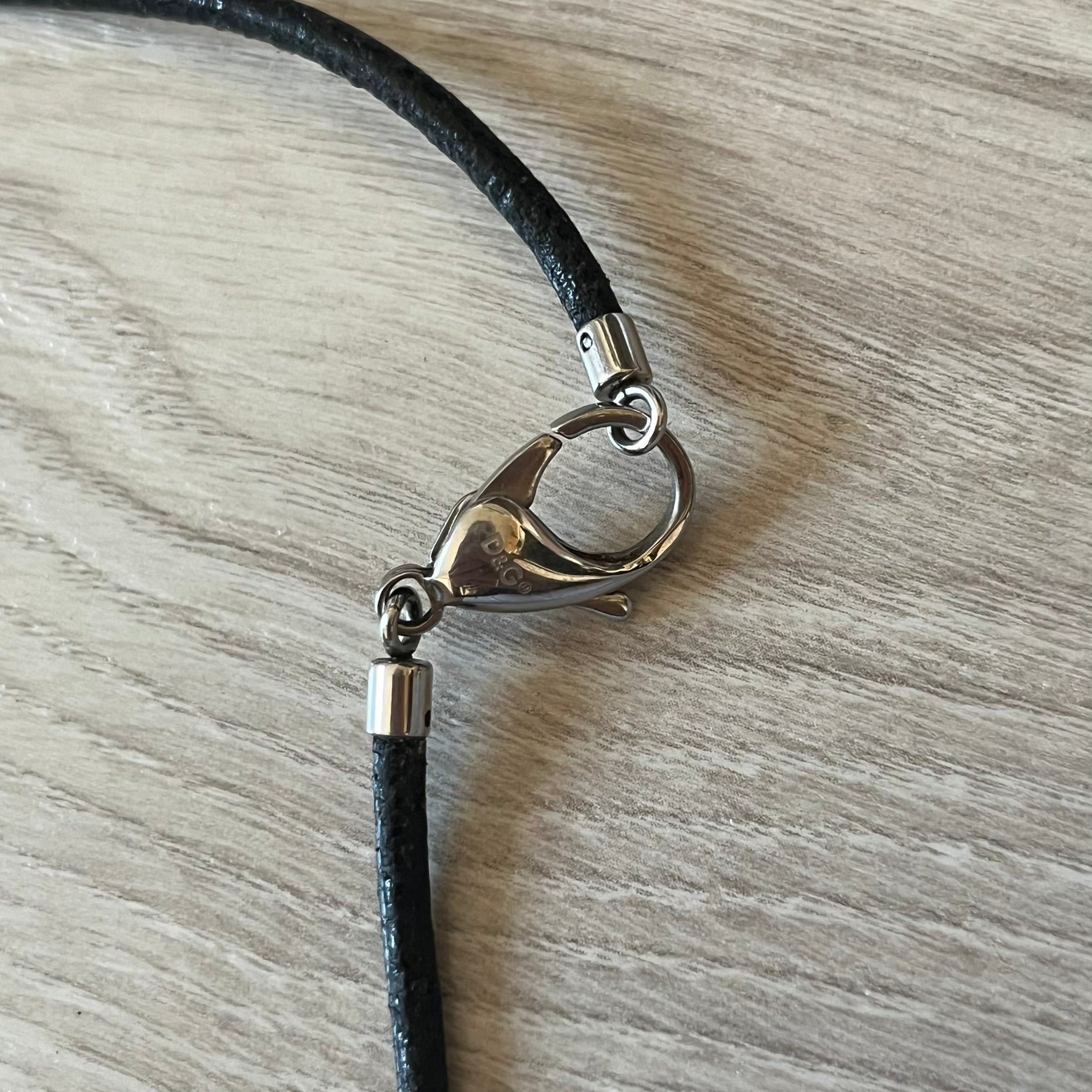Close-up of a black cord with a silver clasp on a wooden surface