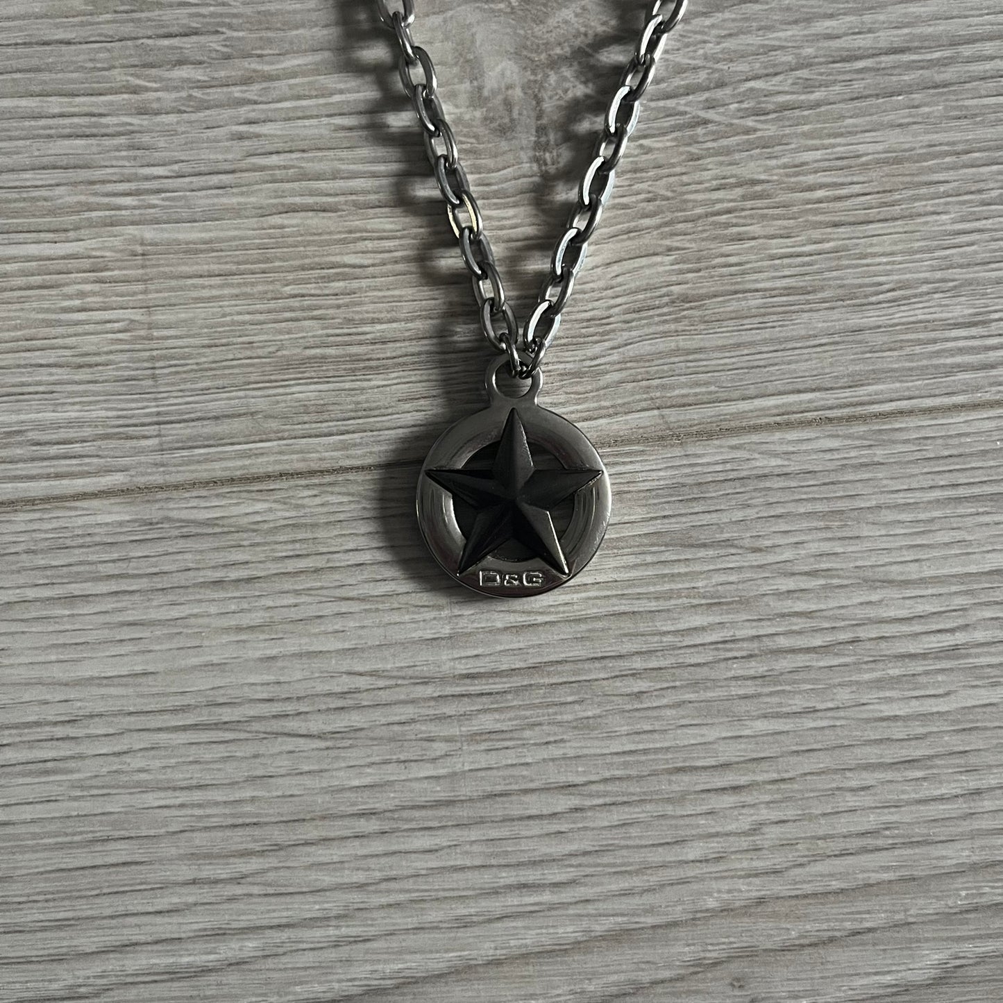 Dolce & Gabbana AW2009 Military Star Dog Tag Necklace in grey. Features a 3D black star mounted on a silver-tone metal circle with an engraved D&G logo at the bottom, suspended from a silver cable chain. Comes complete with original box and tags.