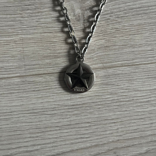 Dolce & Gabbana AW2009 Military Star Dog Tag Necklace in grey. Features a 3D black star mounted on a silver-tone metal circle with an engraved D&G logo at the bottom, suspended from a silver cable chain. Comes complete with original box and tags.