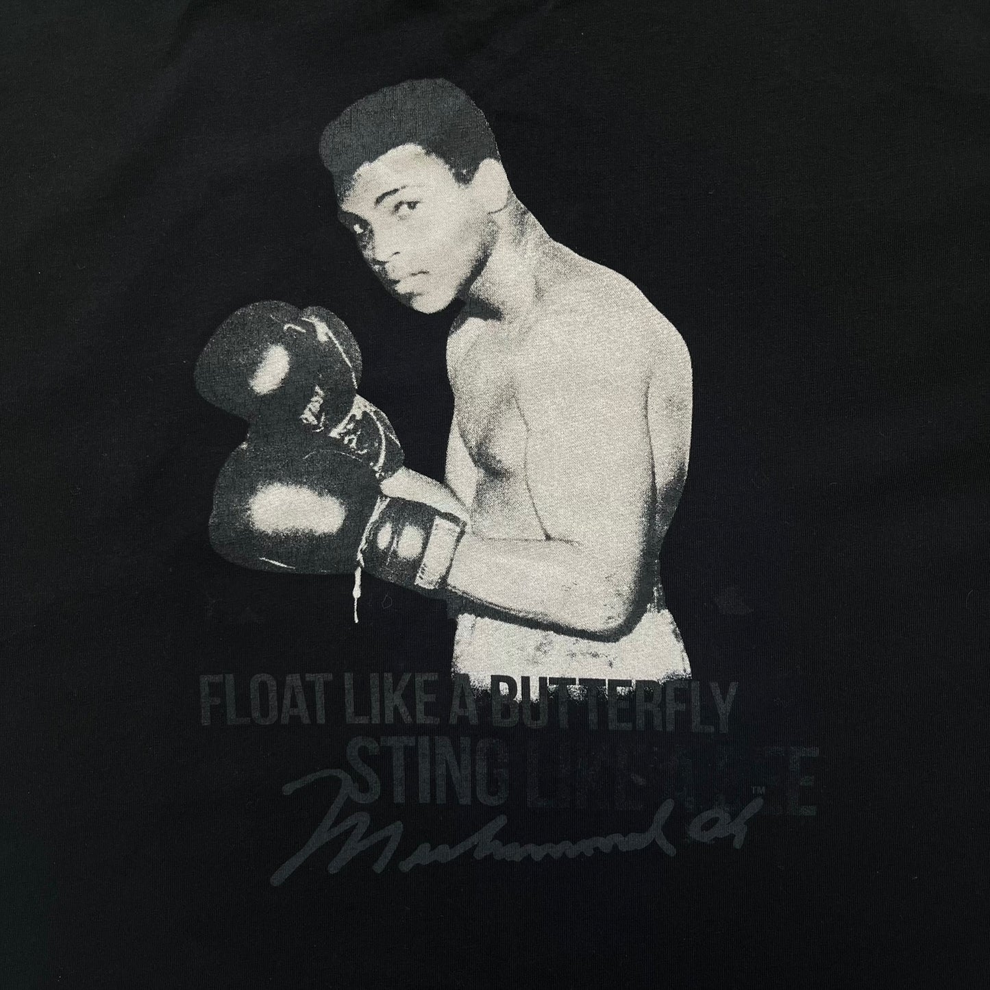  Dolce &amp; Gabbana Muhammad Ali Black Tee is a black T-shirt made in Italy from 100% cotton. The front features a grayscale portrait of Muhammad Ali. Beneath the image is the quote “float like a butterfly sting like a bee” along with a Muhammad Ali signature. 