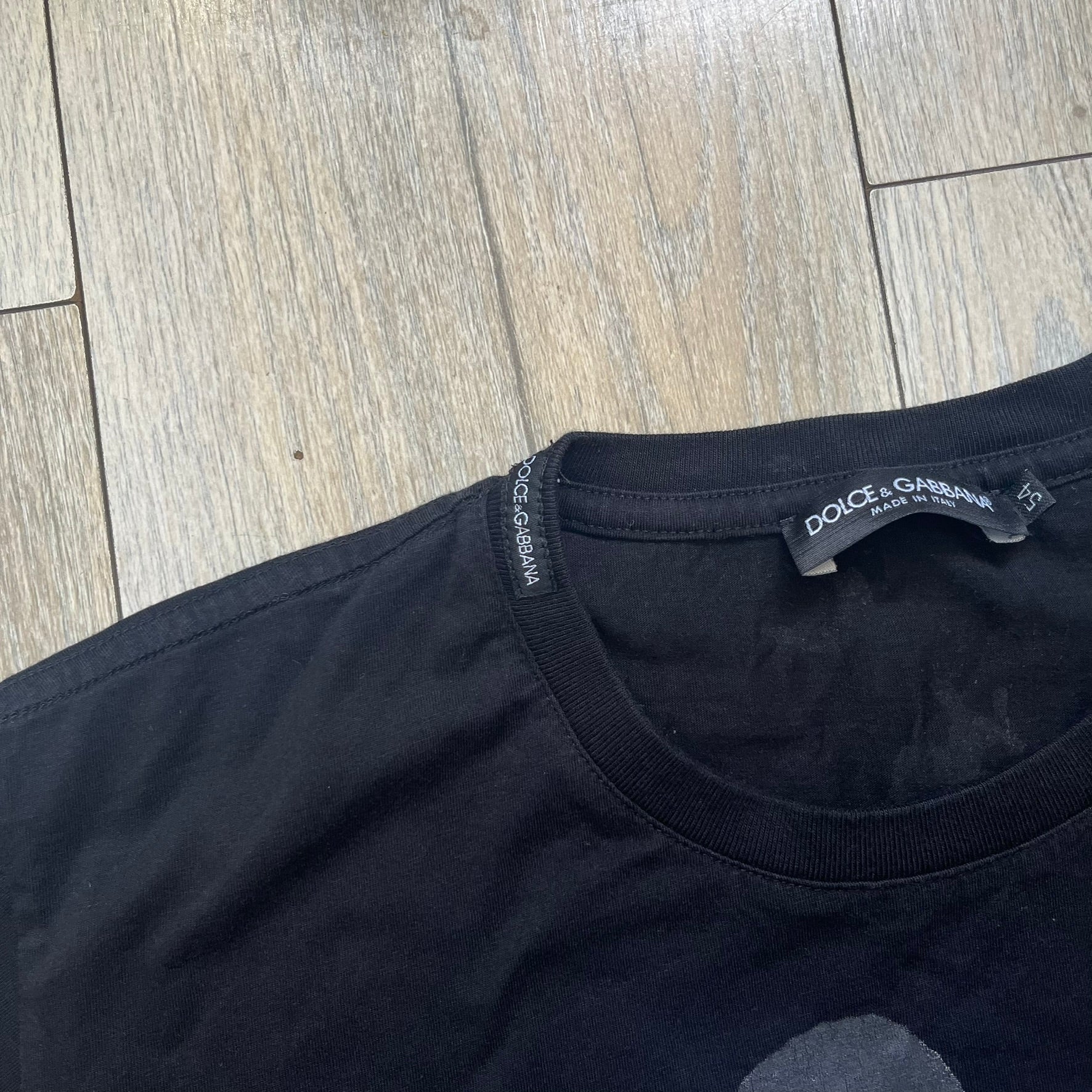 Dolce &amp; Gabbana Muhammad Ali Black Tee is a black T-shirt made in Italy from 100% cotton. The front features a grayscale portrait of Muhammad Ali. Beneath the image is the quote “float like a butterfly sting like a bee” along with a Muhammad Ali signature. 