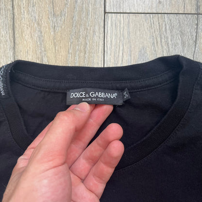  Dolce &amp; Gabbana Muhammad Ali Black Tee is a black T-shirt made in Italy from 100% cotton. The front features a grayscale portrait of Muhammad Ali. Beneath the image is the quote “float like a butterfly sting like a bee” along with a Muhammad Ali signature. 