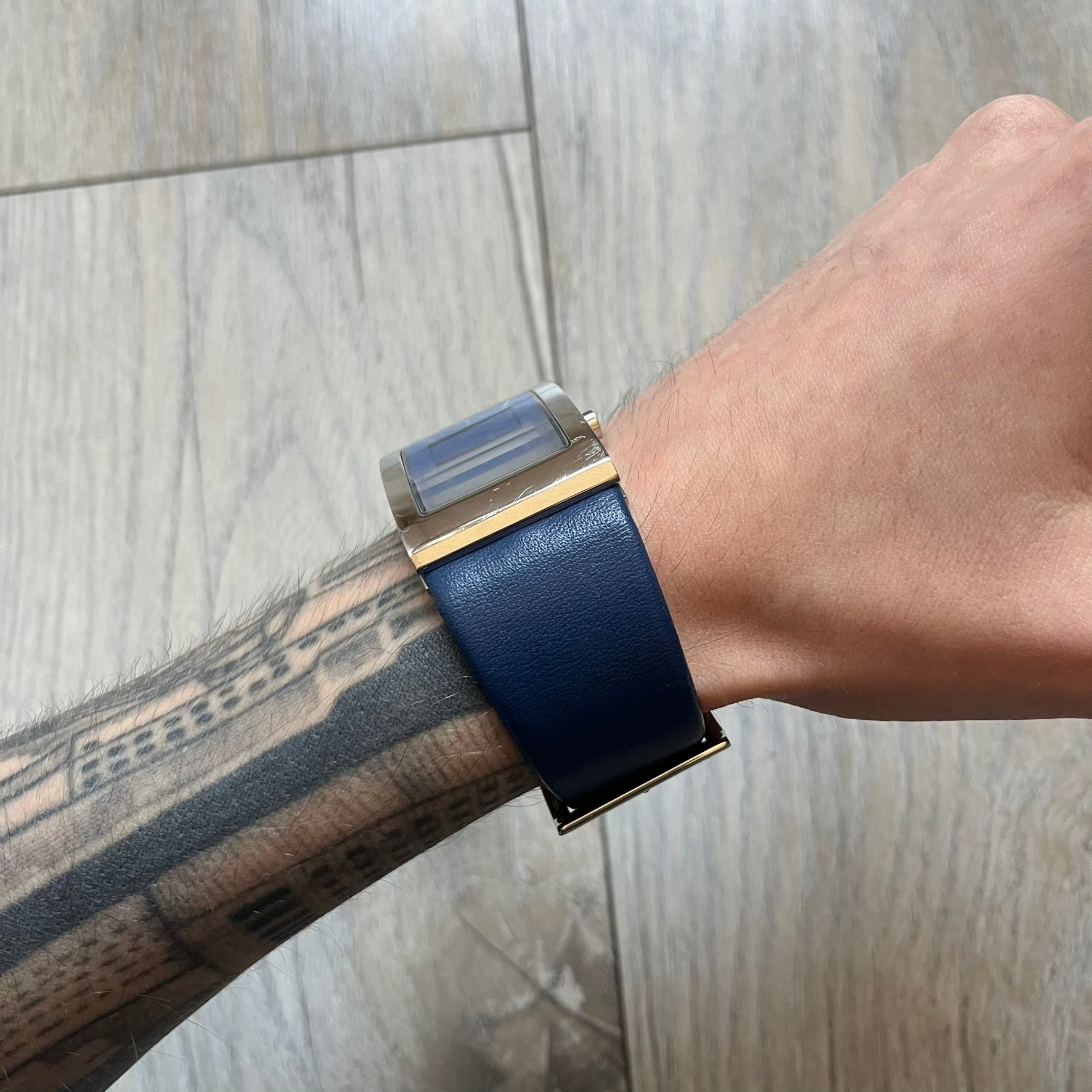 Dolce & Gabbana Navy & Silver Analog Watch features a silver-tone case with a navy dial and matching navy leather strap. The dial has a minimal design with silver hands, a small D&G logo, and a day-date window. The side of the case includes a raised Dolce & Gabbana logo, while the inside of the leather strap is stamped with D&G branding.