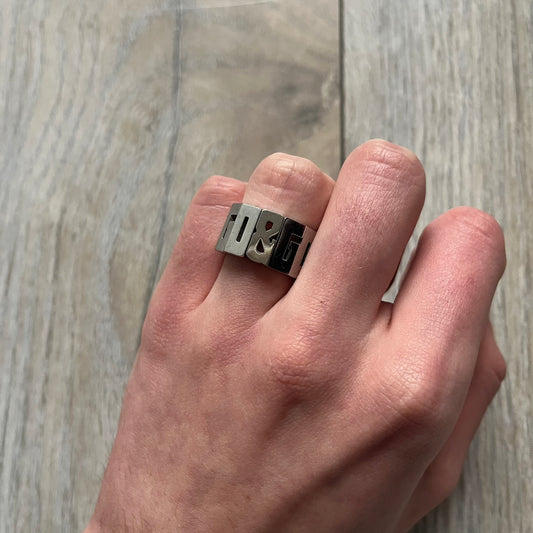 Dolce & Gabbana Overlap DJ0538 Ring is a stainless steel ring constructed entirely from cutout D&G letters. The design features 12 letters forming 4 repeating D&G sets, with each letter’s inner spaces incorporated into the openwork structure