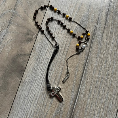 Dolce &amp; Gabbana Pearl Brown Rosary Necklace from the 2000s era. The necklace features a silver-tone metal cross with a D&amp;G logo, connected via a black leather link to a metal chain with alternating brown and yellow pearl-style beads. Rosary-style construction with mixed materials including metal, leather, and resin pearls. Comes complete with the big dustbag.