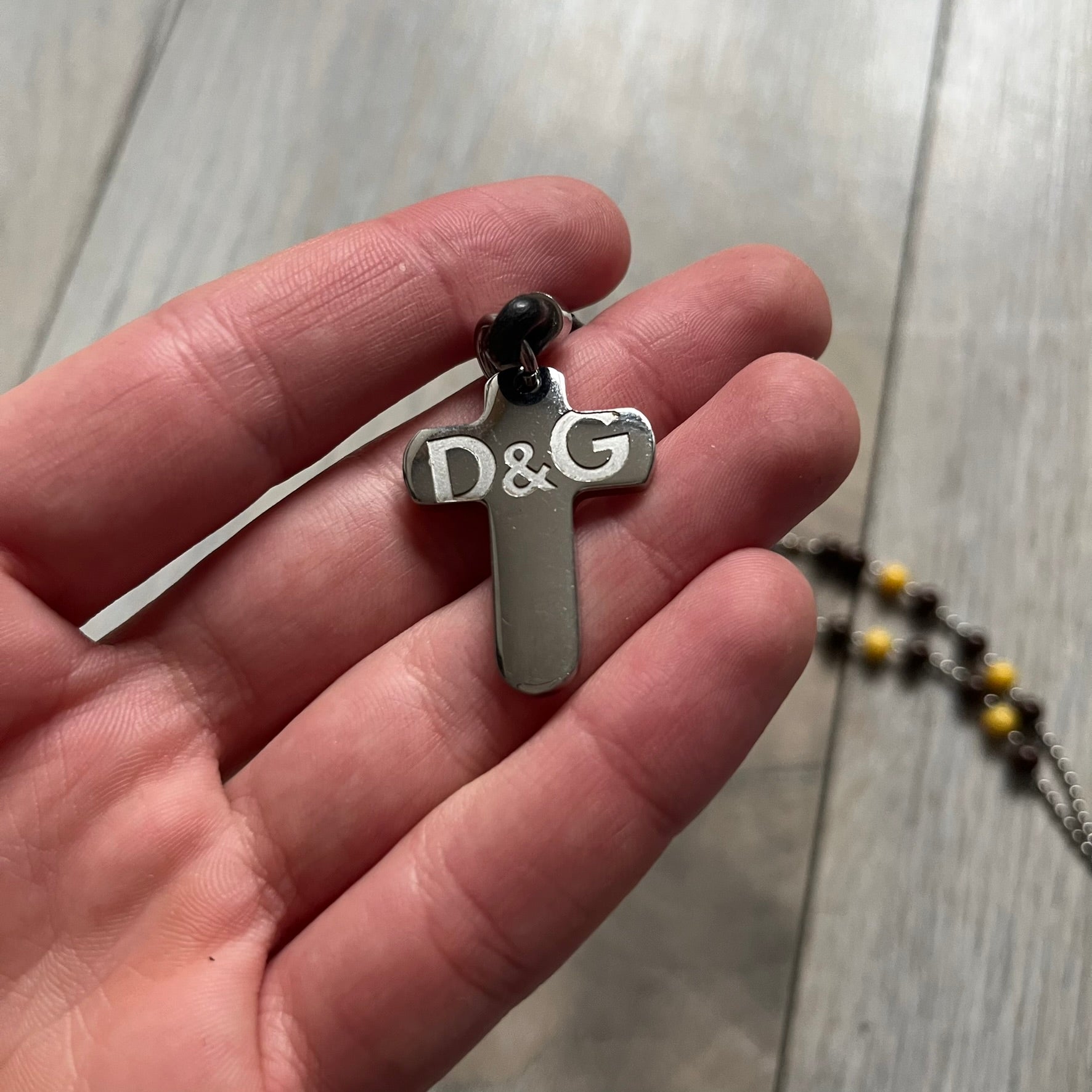 Dolce &amp; Gabbana Pearl Brown Rosary Necklace from the 2000s era. The necklace features a silver-tone metal cross with a D&amp;G logo, connected via a black leather link to a metal chain with alternating brown and yellow pearl-style beads. Rosary-style construction with mixed materials including metal, leather, and resin pearls. Comes complete with the big dustbag.