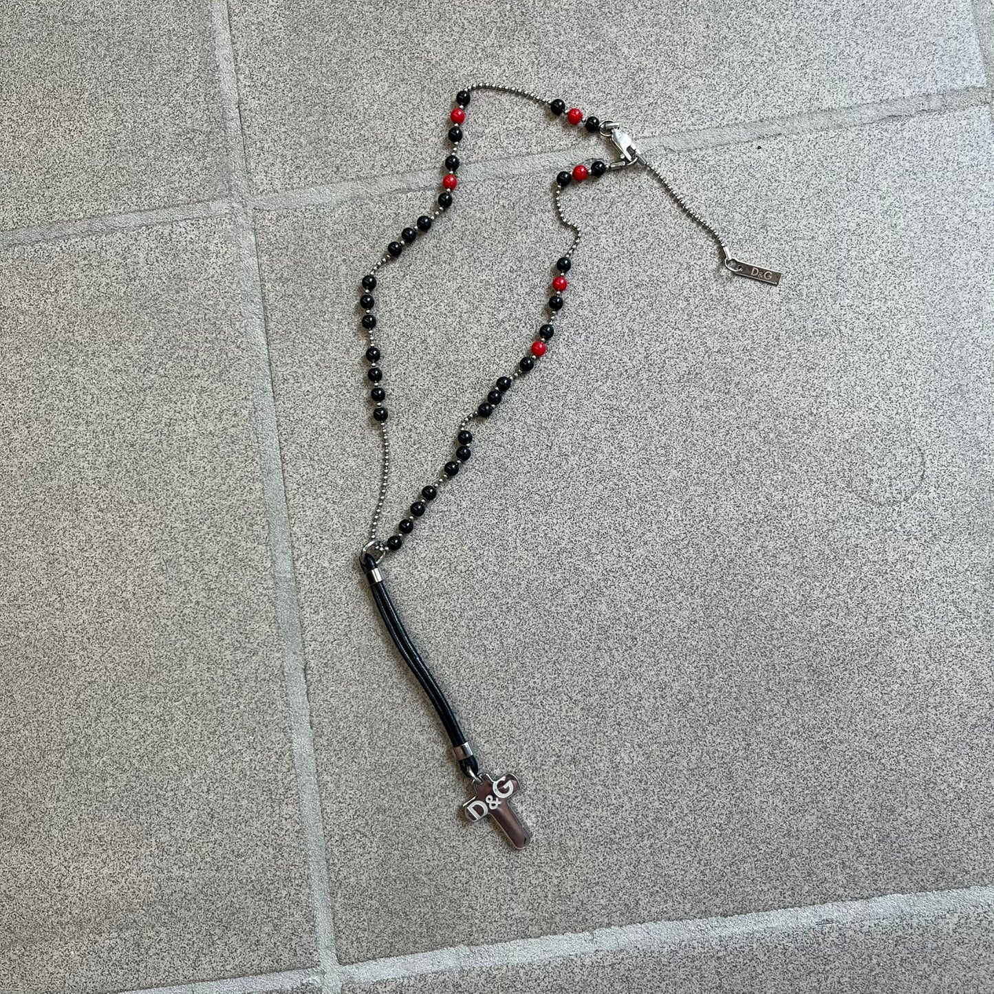 Dolce &amp; Gabbana Pearl Red/Black Rosary Necklace from the 2000's era. The necklace features a silver-tone metal cross with a D&amp;G logo, connected via a black leather link to a metal chain with alternating red and black pearl-style beads. Rosary-style construction with mixed materials including metal, leather, and resin pearls.&nbsp;