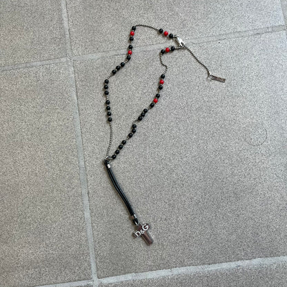 Dolce &amp; Gabbana Pearl Red/Black Rosary Necklace from the 2000's era. The necklace features a silver-tone metal cross with a D&amp;G logo, connected via a black leather link to a metal chain with alternating red and black pearl-style beads. Rosary-style construction with mixed materials including metal, leather, and resin pearls.&nbsp;