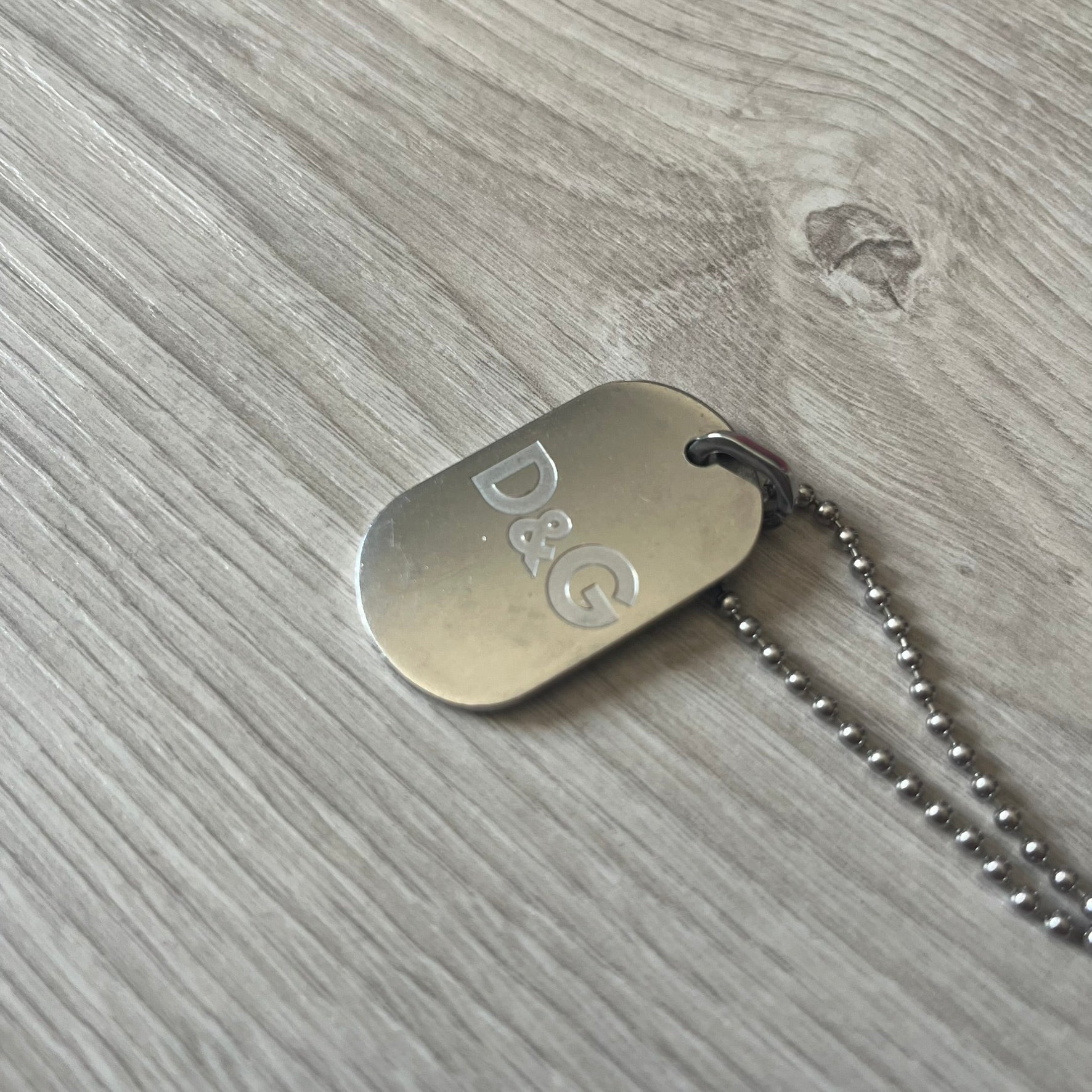 Dolce & Gabbana plain logo dog tag necklace in silver-tone stainless steel, featuring the iconic D&G logo engraved on a sleek tag. Suspended on a classic ball chain with a regulated size. A versatile accessory that combines minimal branding with everyday wearability.