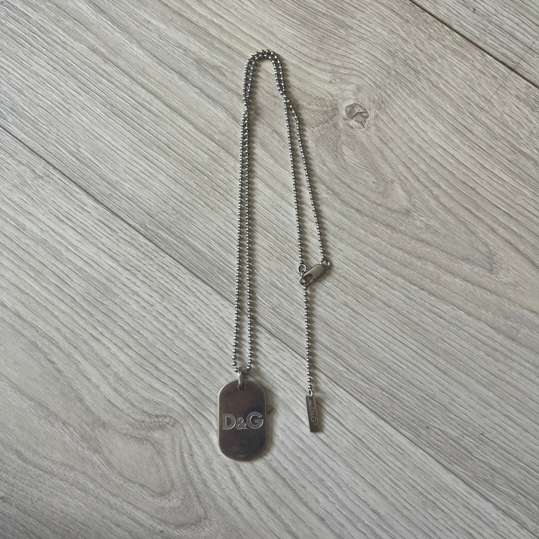 Dolce & Gabbana plain logo dog tag necklace in silver-tone stainless steel, featuring the iconic D&G logo engraved on a sleek tag. Suspended on a classic ball chain with a regulated size. A versatile accessory that combines minimal branding with everyday wearability.