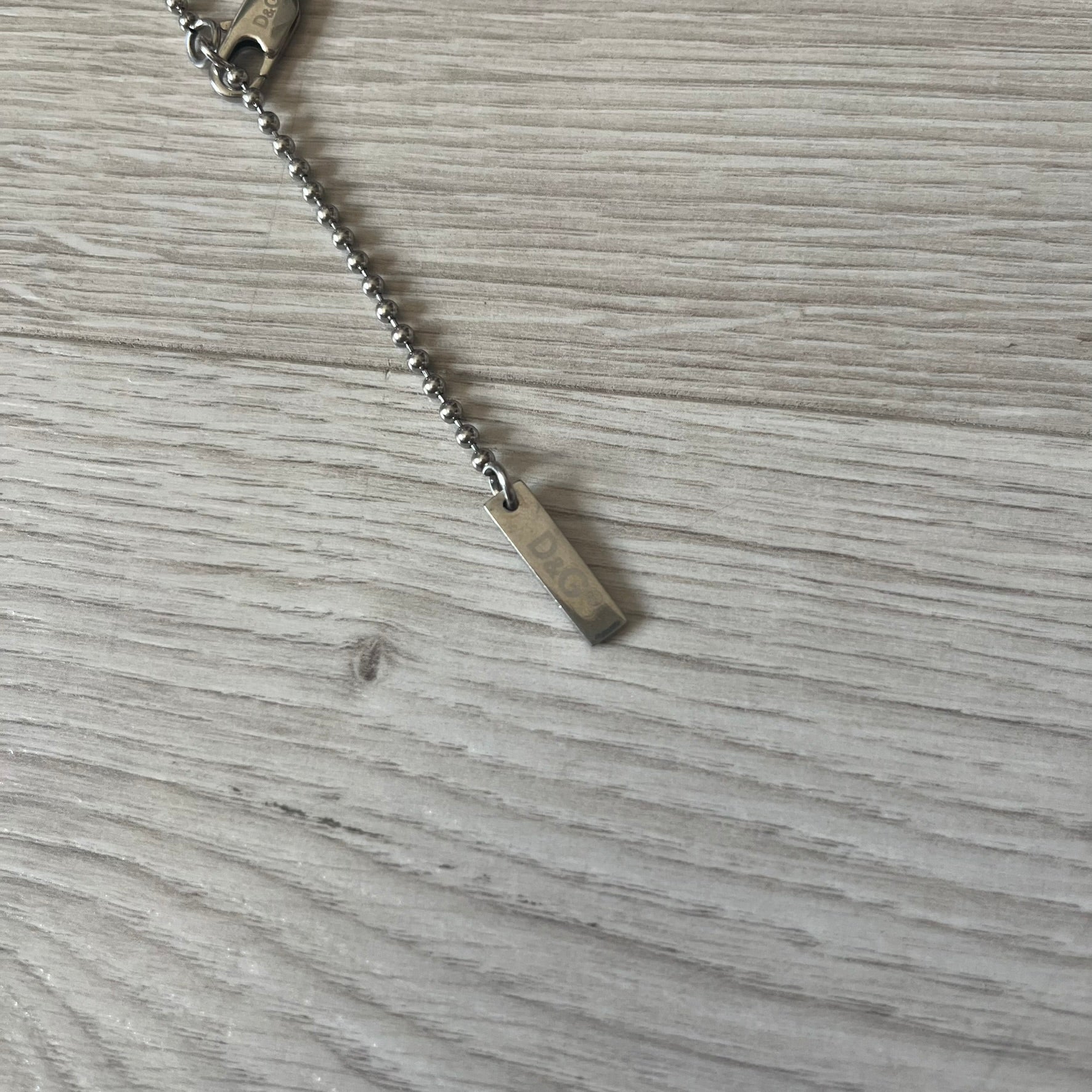 Dolce & Gabbana plain logo dog tag necklace in silver-tone stainless steel, featuring the iconic D&G logo engraved on a sleek tag. Suspended on a classic ball chain with a regulated size. A versatile accessory that combines minimal branding with everyday wearability.