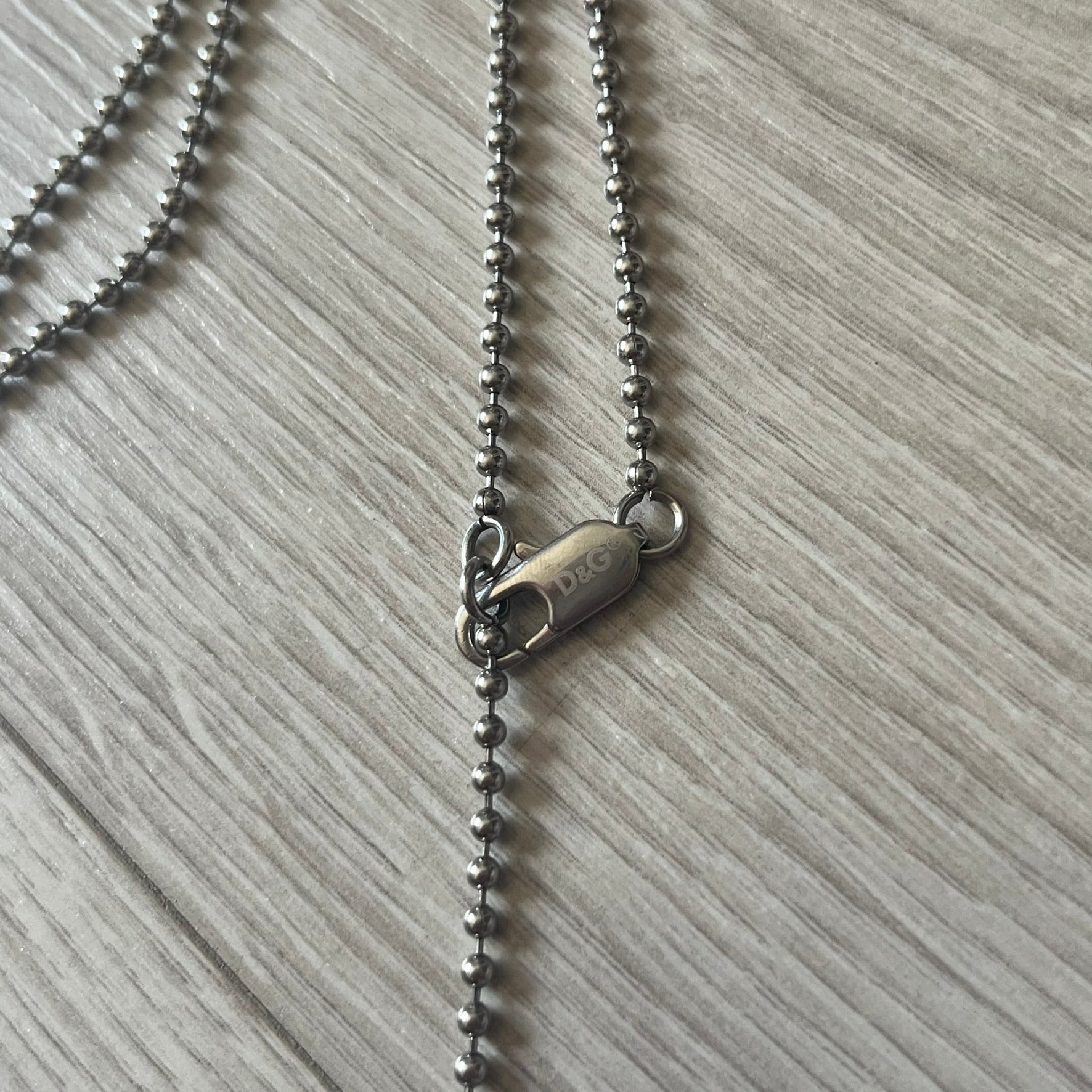 Dolce & Gabbana plain logo dog tag necklace in silver-tone stainless steel, featuring the iconic D&G logo engraved on a sleek tag. Suspended on a classic ball chain with a regulated size. A versatile accessory that combines minimal branding with everyday wearability.