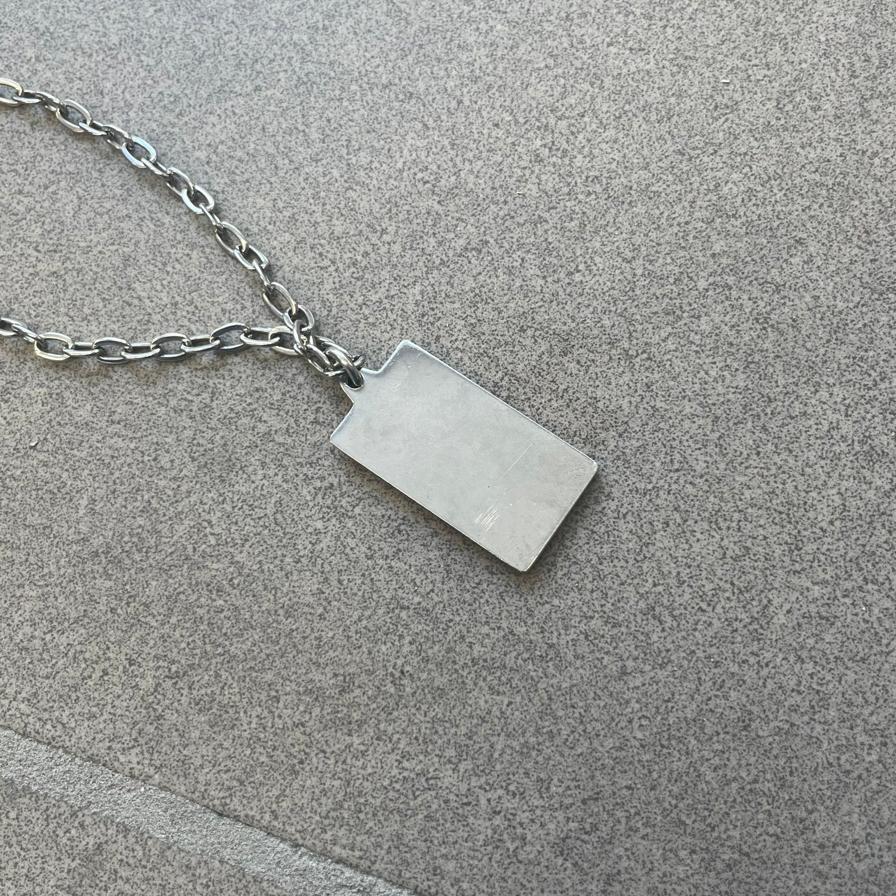 Dolce &amp; Gabbana Propaganda Dog Tag Necklace, featuring a silver stainless steel square tag with four visible screws and the D&amp;G logo engraved on the front. The tag hangs from a durable cable chain, combining sturdy construction with clean, industrial-inspired detailing.