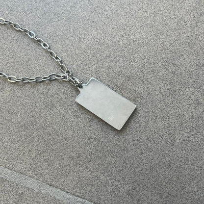 Dolce &amp; Gabbana Propaganda Dog Tag Necklace, featuring a silver stainless steel square tag with four visible screws and the D&amp;G logo engraved on the front. The tag hangs from a durable cable chain, combining sturdy construction with clean, industrial-inspired detailing.