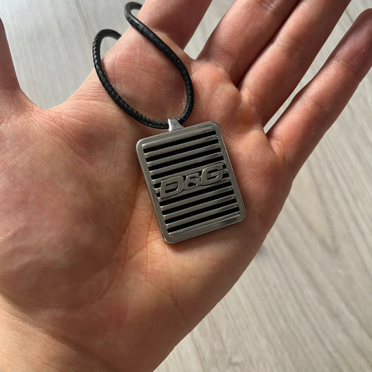 Silver pendant with 'DG' logo held in a hand against a neutral background