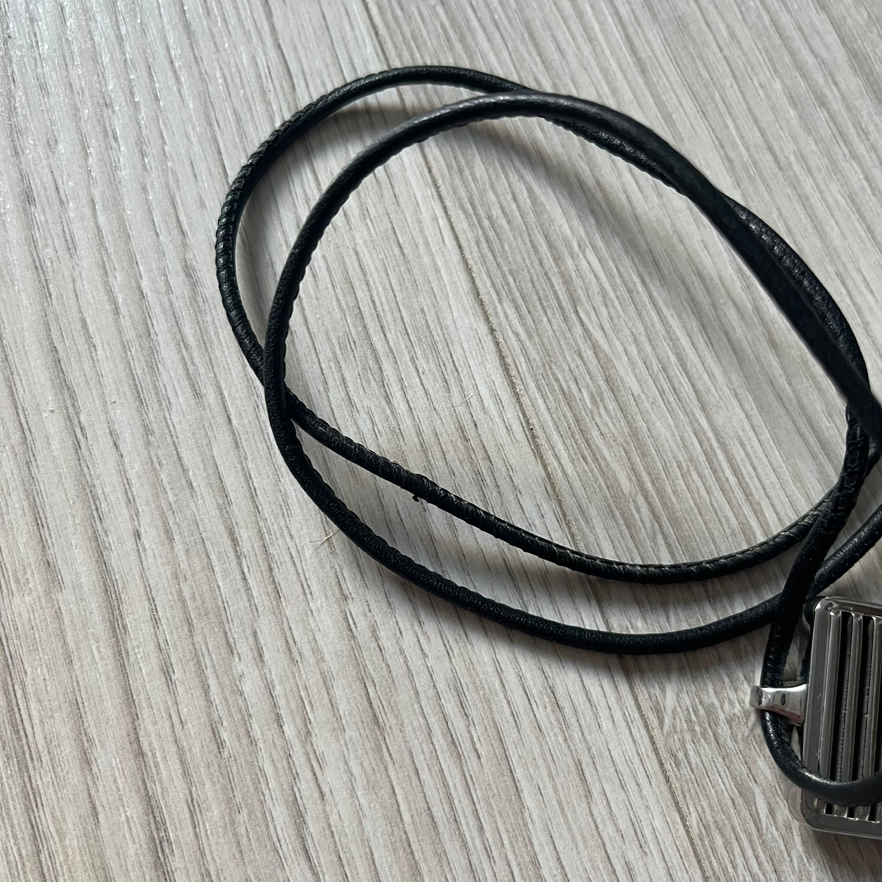 Black leather cord with a metal clasp on a gray wooden surface