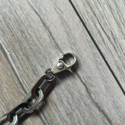 Dolce &amp; Gabbana Razorblade Sample Bracelet is a stainless steel chain bracelet with large interlocking links and a central razor blade-shaped pendant matching the link size. One side of the pendant is engraved with the D&amp;G logo, while the opposite side features small “SAMPLE” text. The bracelet secures with a lobster clasp engraved with Dolce &amp; Gabbana logos.